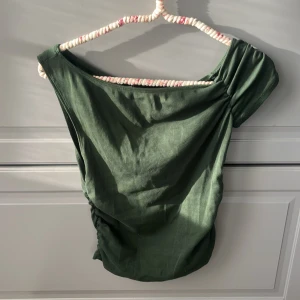 Grön omlott topp från Zara - Mörkgrön topp från Zara med omlottkänsla och snygg rynkning på ena sidan. Asymmetrisk offshoulder-design och lätt stretchigt material som sitter skönt. Perfekt för dig som gillar en unik och trendig look. Kom privat för en bild när den är på!😌😇