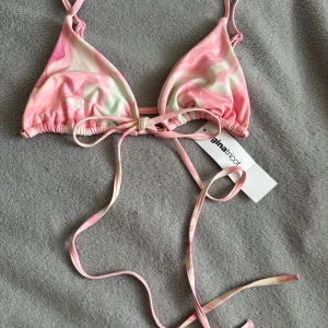 Rosa mönstrad bikini från Gina Tricot - Supersöt trekantsbikini från Gina Tricot i rosa, vitt och ljusgrönt swirlmönster. Bikinin har smala axelband och knytning både i ryggen och nacken för perfekt passform. Materialet är mjukt och stretchigt, perfekt för sommardagar på stranden. Man kan knyta den på många olika sett tack bare dess långa band!🎀 