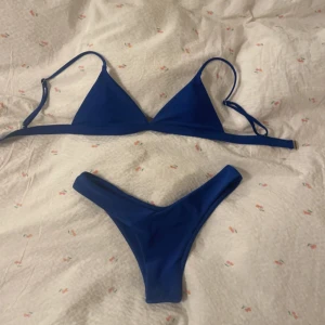 Blå trekantsbikini med låga trosor - Snygg blå bikini med klassisk trekants-bh och justerbara axelband. Underdelen har en låg midja och v-formad skärning framtill. Materialet är stretchigt, perfekt för strand eller pool. Enkel och stilren design utan mönster eller extra detaljer. Underdelen är storlek M och överdelen storlek S🫶🏼 köptes på vinted och är aldrig använd av mig men vet ej om förra ägaren använt den eller inte tyvärr💞
