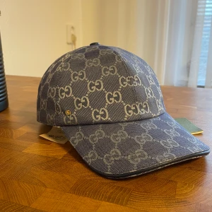 Gucci keps Dubai blå - Snygg keps från Gucci i blått med klassiskt GG-mönster över hela kepsen. Justerbar rem baktill i skinn och insida i ljus bomull. Perfekt accessoar för att lyfta din outfit med en lyxig touch.