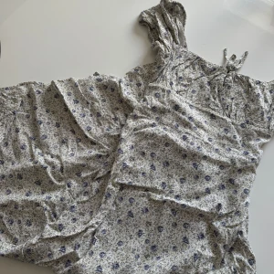 Blommig långklänning  - Supersöt långklänning med blått blommönster på ljus botten. Klänningen har en defekt (vilken man kan se på tredje sista bilden) där tyget har typ gått upp vid dragkedjan, inte något som speciellt syns men absolut något att lägga märke till!