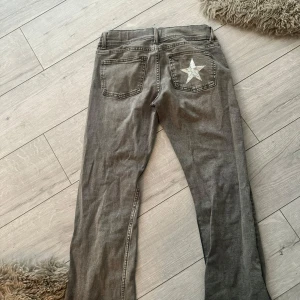 Grå jeans med stjärna på bakfickan - Snygga grå jeans med en vit stjärna på ena bakfickan. Byxorna har klassisk femficksdesign, raka ben och normal passform. Perfekta för dig som vill ha en cool detalj på dina jeans. Materialet är mjukt och bekvämt denim. Storlek 170