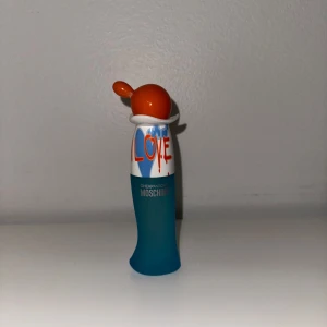 Moschino Cheap and Chic I Love Love - Parfymflaska från Moschino Cheap and Chic I Love Love med lekfull design. Flaskan är blå i frostat glas med vit och orange plastkork som har en unik, rund form. Texten 'LOVE' i rött och blått ger en färgglad och ungdomlig känsla.