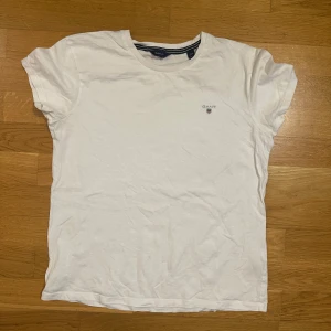 Vit t-shirt från Gant - Klassisk vit t-shirt från Gant med liten broderad logga på bröstet. T-shirten har rund halsringning och korta ärmar. Perfekt basic-plagg i mjuk bomull som funkar till allt.