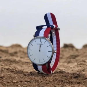 Chronos klocka med randigt band - Stilren klocka från Chronos med vitt ur och minimalistisk design. Bandet är randigt i blått, vitt och rött och ger en sportig vibe. Boetten är i silverfärgad metall och urtavlan är enkel utan siffror. Perfekt accessoar för dig som gillar klassisk men färgglad stil.