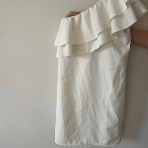 Vit one shoulder klänning med volang - Klänningen har ett bälte i midjan. 