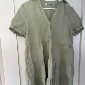 Zara klänning  - Superfin ljusgrön klänning från Zara. Den har v-ringning, korta ärmar och knappar framtill. Klänningen har en avslappnad passform med volanger i flera lager som ger en luftig känsla. Perfekt för varma dagar och enkel att styla.