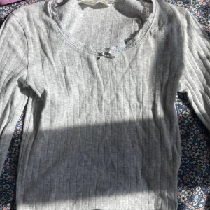 Grå långärmad topp med spets! - Supersöt grå långärmad topp från H&M med spetskant vid halsen och en liten rosett framtill. Perfekt för lager-på-lager och chill dagar!💞
