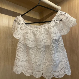 Vit offshoulder spetsblus  - Superfin vit offshoulder blus från coolcat i storlek S. Blusen är helt täckt av spets med blommiga detaljer och har en bred volang runt axlarna. Passar S men också xs. Lite kroppad. 