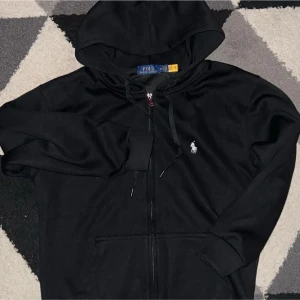 Svarta Polo Ralph Lauren hoodie  - Svart Polo Ralph Lauren hoodie med dragkedja – helt ny! Snygg zip-up hoodie i storlek M, passar även dig som har S. Inga fläckar, inga hål – i toppskick! ☔️ Originaltags medföljer. Perfekt för dig som vill ha stil och kvalitet 🔥💯 