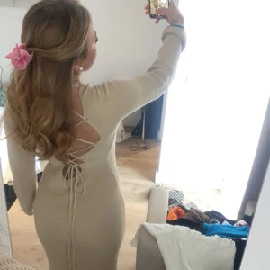 Beige ribbad långklänning med snörning - Supersnygg beige långklänning i ribbat material med öppen rygg och snörningsdetalj  bak. Klänningen har lång ärm och figurnära passform som framhäver siluetten. Perfekt för dig som vill sticka ut med en trendig och elegant look. Används en gång!
