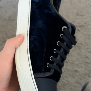 Svarta mockasneakers från Lanvin - Snygga svarta sneakers från Lanvin med ovandel i lyxig mocka och detaljer i svart läder. Skorna har en vit, robust sula och svarta snören för en clean look. Perfekta för dig som gillar stilrena och exklusiva sneakers.
