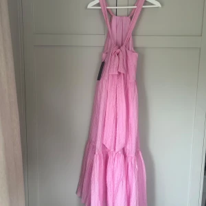 Midsommar/sommar klänning  - !!! Aldrig använd !!! Superfin unik rosa långklänning som jag köpte förra året från en liten butik på Sandhamn. Klänningen har breda axelband, volangig kjol och en snygg knytning i ryggen. Klänningen har aldrig använts eftersom jag köpte fel storlek och det ej gick att lämna tillbaka. Passar perfekt till midsommar, sommarfester och andra tillställningar💓 orginalpris 1400 