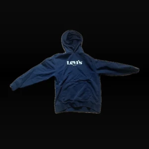 Mörkblå Levi's hoodie med tryck - Säljer en mörkblå hoodie från Levi's med vit logga på bröstet. Klassisk känguruficka framtill, huva och ribbade muddar. Perfekt för dig som gillar en avslappnad och stilren look. Materialet är mjuk bomullsmix som känns skön mot huden.