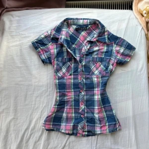 Rutig kortärmad skjorta Atmosphere - Kortärmad skjorta från Atmosphere i färgglatt rutigt mönster med blå, rosa, grön och vit. Skjortan har figurnära passform, två bröstfickor och knappar framtill. Perfekt för dig som gillar en avslappnad men ändå snygg stil.