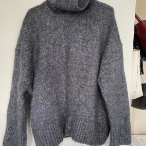 Grå stickad polotröja - Mysig grå stickad polotröja med oversized passform och långa ärmar. Tröjan har en hög polokrage och breda ribbade muddar vid ärmslut och nederkant.