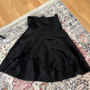 Svart vid kjol i pälsimitation - Säljer en svart, vid kjol i pälsimitation med hög midja. Kjolen har en mjuk och fluffig känsla och passar perfekt när du vill sticka ut lite extra. Enkel att styla med både boots och sneakers.