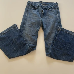 Blå bootcut jeans från 7 For All Mankind - Snygga blå jeans från 7 For All Mankind med bootcut passform och låg midja. Jeansen har klassisk femficksdesign, broderade bakfickor och en lätt tvättad look. Perfekta för dig som gillar en avslappnad men trendig stil.