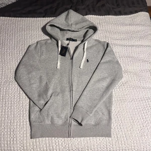 Grå hoodie från Polo Ralph Lauren - Ljusgrå full zip hoodie från Polo Ralph Lauren. Storlek M. Nyskick!