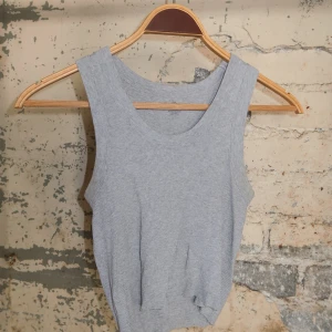 Ljusgrå ribbad linnetopp - Säljer en enkel och stilren ljusgrå linnetopp med ribbad struktur. Toppen är ärmlös och har en rund halsringning, perfekt för en avslappnad look. Passar snyggt till både jeans och kjol.