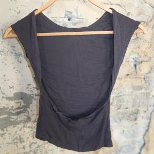 Svart ärmlös linnetopp med öppen rygg - En svart, tight och ärmlös linnetopp med djup öppen rygg. Toppen har en enkel och stilren design med breda axelband och rundad halsringning. Perfekt för att skapa en cool och minimalistisk look.