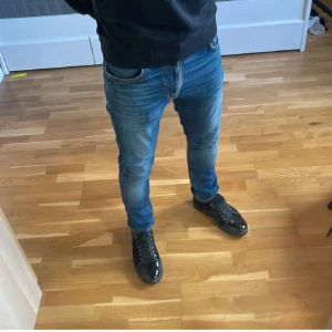 Blå jeans från Nudie Jeans - Säljer ett par klassiska blå jeans från Nudie Jeans med snygg tvätt och diskreta slitningar. Modellen har normal passform och raka ben. Jeansen är i bomull och har Nudie-loggan på bakfickan. Perfekta till sneakers och hoodie.