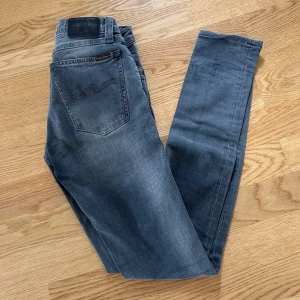 Gråa jeans från Nudie jeans - Säljer ett par snygga gråa Nudie jeans i storlek W25 L32. Jeansen är i väldigt bra skick.
