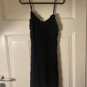 Svart klänning från H&M - Svart kortklänning från H&M med smala axelband och struktur i tyget. Klänningen är o storlek m men är stretchig så passar både mindre och större.