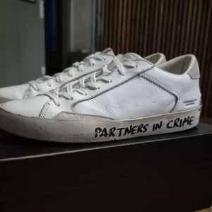 Skor från Crime London - Snygga vita sneakers från Crime London med 'PARTNERS IN CRIME' på sulan. Skorna har snörning, detaljer i mocka vid hälen och är gjorda i skinn. Storlek 41 men passar även 42 mycket bra. Det finns låda också! 