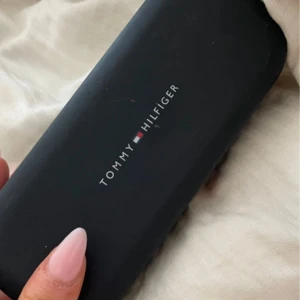 Svarta solglasögon från Tommy Hilfiger - Snygga svarta solglasögon från Tommy Hilfiger med en klassisk design. De har en elegant svart båge och kommer i ett stilrent fodral med märkets logga. Perfekta för att ge en touch av stil till din outfit.