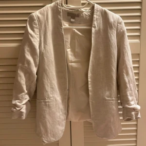 Beige kavaj - Snygg beige kavaj med normal passform och 3/4 ärmar. Tillverkad i ett lätt och bekvämt material, perfekt för både vår och höst. Kavajen har en stilren design utan knappar utan något annat som håller fast den och två fickor framtill.