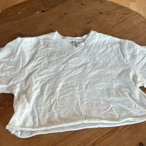 Vit croppad t-shirt - Säljer en vit croppad t-shirt med korta ärmar. T-shirten har en enkel design och är gjord i ett mjukt material.