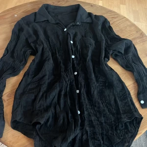 Svart skjorta med knappar - Snygg svart skjorta med krage och knappar framtill. Skjortan har en lös passform och är långärmad, 