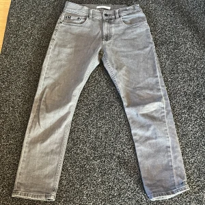 Grå jeans från Calvin Klein - Snygga grå jeans från Calvin Klein med klassisk femficksdesign och dragkedja. De har en rak passform och är perfekta för en stilren look. Märkeslogga på baksidan ger en extra touch av stil.