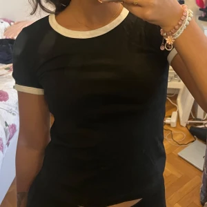 Svart t-shirt med vita detaljer - Snygg svart t-shirt med vita kanter vid hals och ärmar. Perfekt för en casual look. Passar bra till jeans eller shorts.