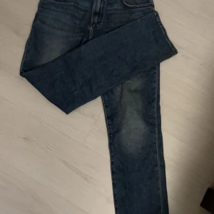 Blå jeans från Lee - Snygga blå jeans från Lee med klassisk femficksdesign och en läderpatch med logotyp baktill. Jeansen har en rak passform och är perfekta för en avslappnad stil. De är tillverkade i slitstarkt denim och har en bekväm midwaist. 30/32