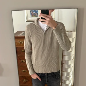 Beige ribbad tröja från Jack & Jones - Säljer en stilren beige ribbad tröja från Jack & Jones. Tröjan har en dragkedja vid halsen och långa ärmar, perfekt för en avslappnad look. Tillverkad i mjukt material för extra komfort. Storleken är M men passar även den som brukar variera mellan M och L