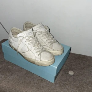 Philippe Model - Säljer ett par stilrena vita sneakers från Philippe Model. Skorna har en klassisk design med snörning och är tillverkade i skinn. Perfekta för en avslappnad och trendig look.