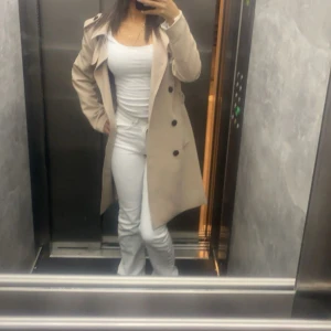 Beige trenchcoat - Snygg beige trenchcoat med klassisk design och knappar framtill. Perfekt för övergångsperioder med sin stilrena look och långa ärmar.