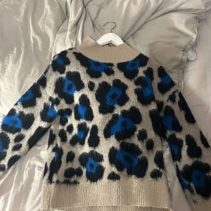Beige leopardmönstrad tröja från Gina Tricot - Säljer en snygg beige tröja från Gina Tricot med ett djärvt leopardmönster i svart och blått. Tröjan har en hög krage och långa ärmar, perfekt för att hålla sig varm och stilren. Passar utmärkt för höst och vinter.