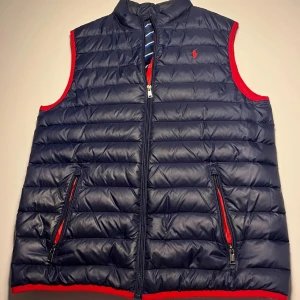 Ralph Lauren dunväst - Säljer denna riktigt snygga mörkblåa dunvästen från Ralph lauren. Varan är i bra skick och perfekt för våren och lite kallare dagar. Storlek S/M. Passar mig bra som är 180. Pris kan diskuteras vid snabb affär 