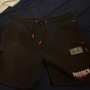 Svarta shorts från Hoodrich - Snygga svarta shorts från Hoodrich med coola detaljer och snörning i midjan. Perfekta för en avslappnad stil. Märkeslogga synlig både fram och bak.
