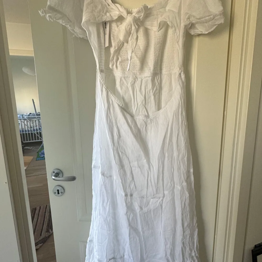 Charmig vit långklänning med puffiga kortärmar och smockdetaljer på överdelen. Klänningen har en söt knytning framtill och är perfekt för somriga dagar. 600kr nypris, aldrig använd.. Mekot.
