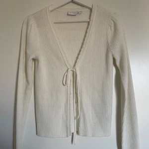 Vit ribbad kofta från VILA - Säljer en superfin vit ribbad kofta från VILA i storlek XS. Koftan har en v-ringad design med knytband framtill och långa ärmar. Använd ett fåtal gånger så den är i fint skick💞 fråga gärna för bilder på!