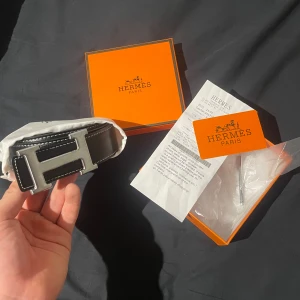 H-bälte  - Snyggt svart skärp med en ikonisk H-formad spänne i silver. Skärpet är tillverkat i skinn och kommer i sin originalförpackning med tillhörande påse och dokumentation. Perfekt för att ge en lyxig touch till din outfit. Jag prioriterar snabba affärer och priset är diskuterarbart. H är lite slitet