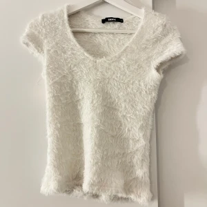 Vit fluffig topp från Bikbok!! - Säljer en supermjuk och fluffig vit topp från Bikbok. Den har en v-ringad design och korta ärmar, perfekt för en stilren look. Använd fåtal gånger!!🎀💕