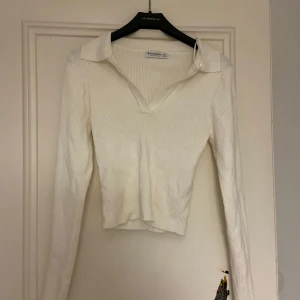 Vit ribbad tröja från Stradivarius - Säljer en stilren vit ribbad tröja från Stradivarius. Tröjan har en v-ringad design med krage och långa ärmar, perfekt för en elegant look. Passar bra till både jeans och kjol.