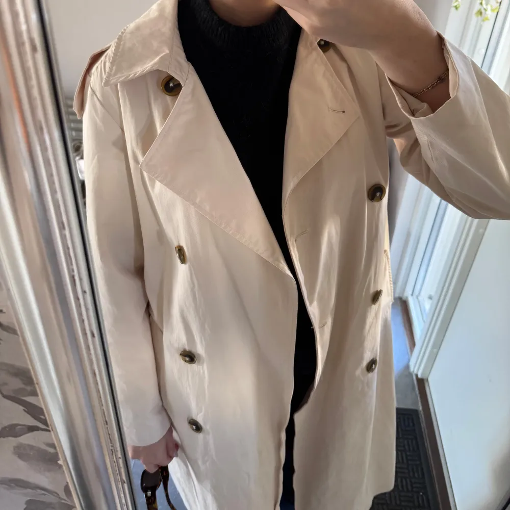 Snygg beige trenchcoat från Object med knappar och bälte i midjan. Jackan har en klassisk design med långa ärmar och en stilren look.. Takit.