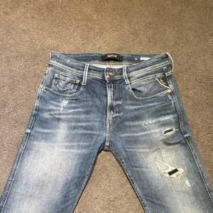 Blå jeans från Replay - Snygga blå jeans från Replay med slitna detaljer och en klassisk femficksdesign. De har en dragkedja och knapp framtill samt en läderpatch på baksidan av midjan. Perfekta för en avslappnad stil. Waist 31 length 34(skulle säga att den passar bättre på folk med  waist 30) 