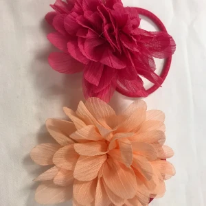 stora blommor hårsnoddar  - Två färgglada hårsnoddar med stora blommor i rosa och persikofärg. Perfekta för att ge en färgklick till din outfit. Blommorna är gjorda av ett lätt och luftigt material som ger en romantisk känsla. Helt ny 